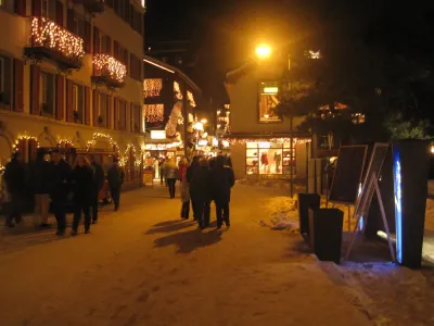 Een dorpsstraat in de sneeuw, 's avonds verlicht door lantaarns